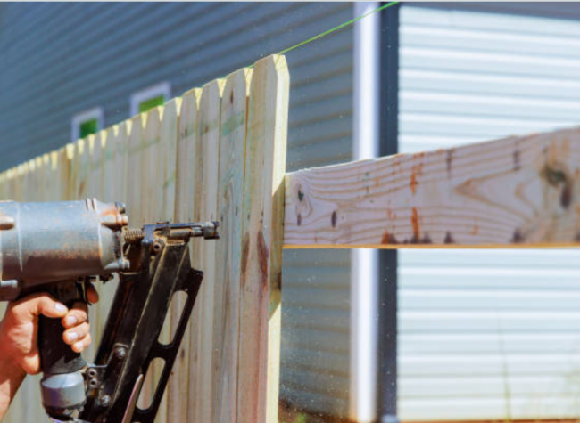 Man Holding a nail gun installing a residential wooden fence.