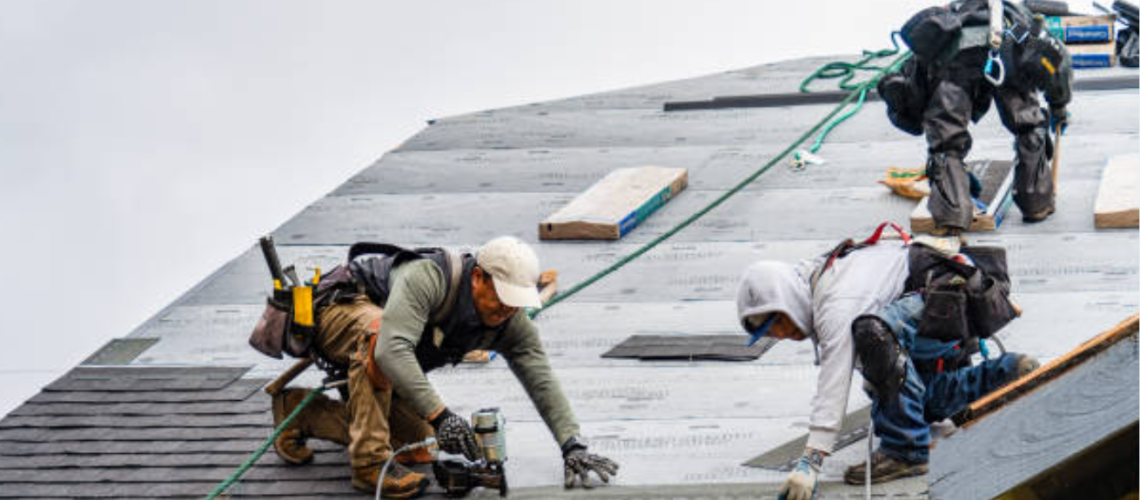 Roofing crew on top of a residential house nailing shingles